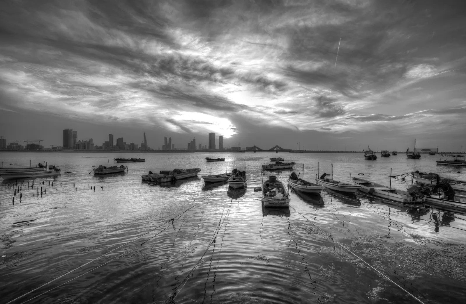 Fishing boats moored in shallow water with the Bahrain skyline under heavy cloud